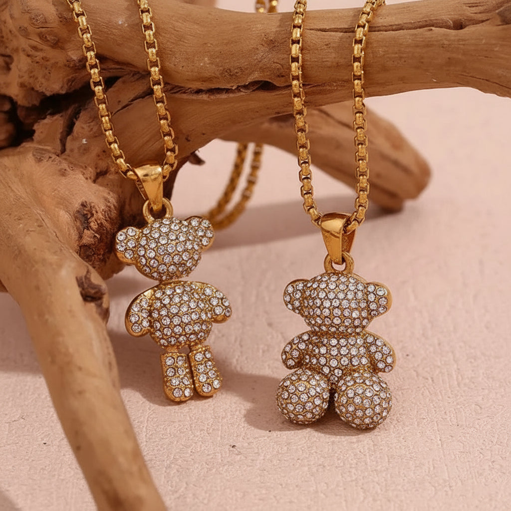 One standing gold teddy bear with inlay stones and one sitting gold teddy bear with inlay stones pendant necklace against a wooden background