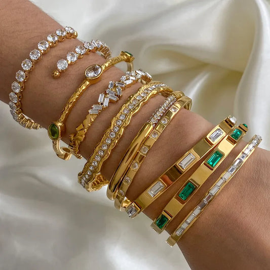 Gold bracelets with gemstones on an arm with a white fabric background