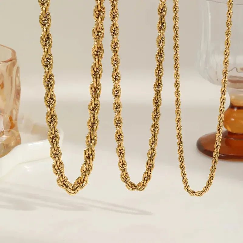 Three gold twisted rope chain necklaces displayed on a white surface with glass decor background