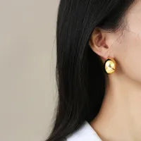 Gold earring worn by a person with dark hair against a neutral background