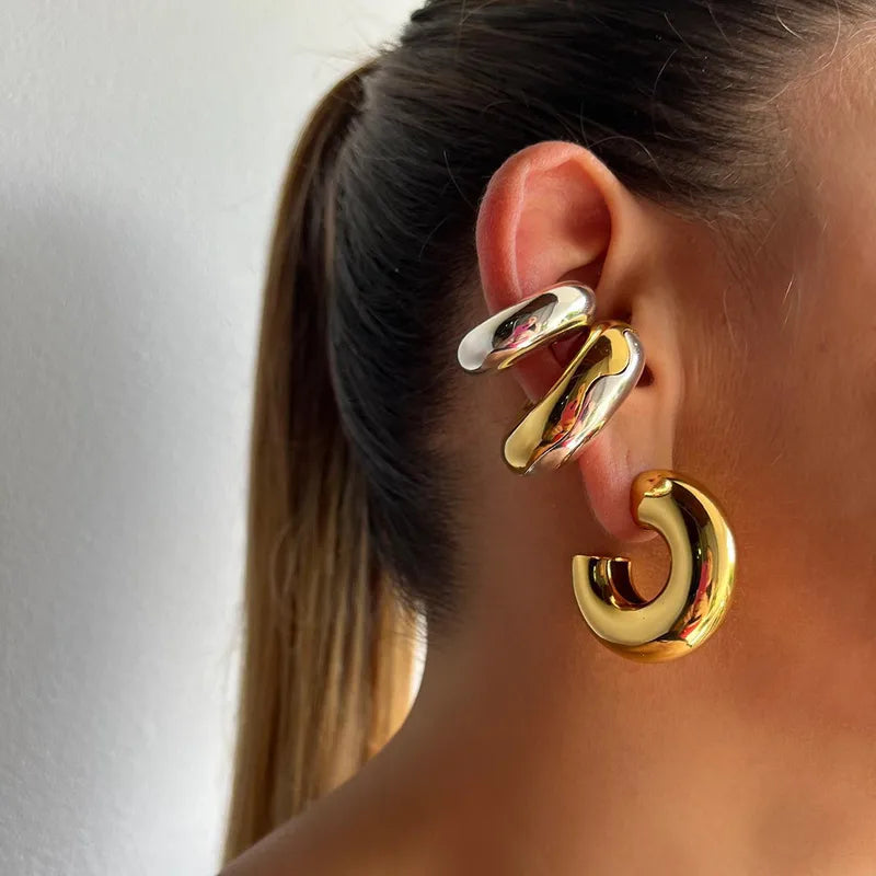 Gold and silver ear cuffs and gold hoop worn by a person with a plain background