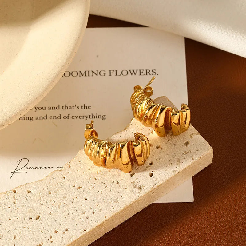 gold c shape stud earrings on a stone background