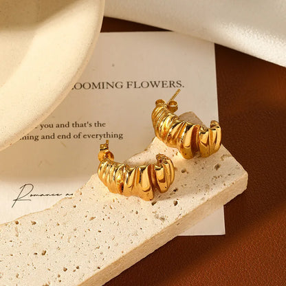 gold c shape stud earrings on a stone background
