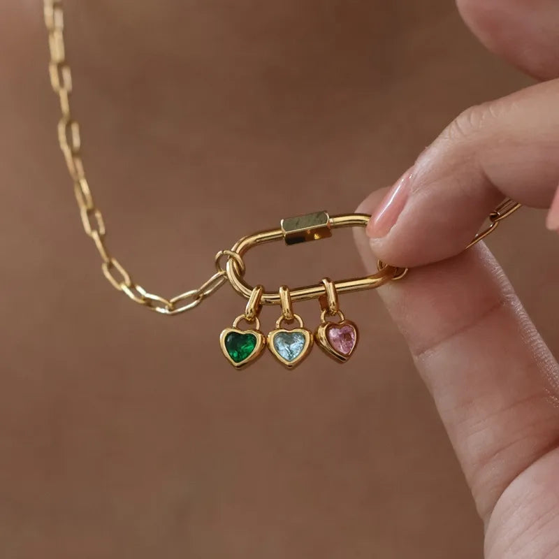 Gold necklace with heart-shaped charms held by a hand against a neutral background