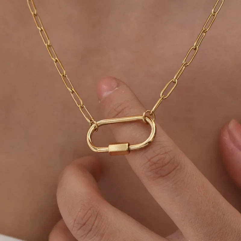 Gold chain necklace with a carabiner clasp held by a hand against a neutral background