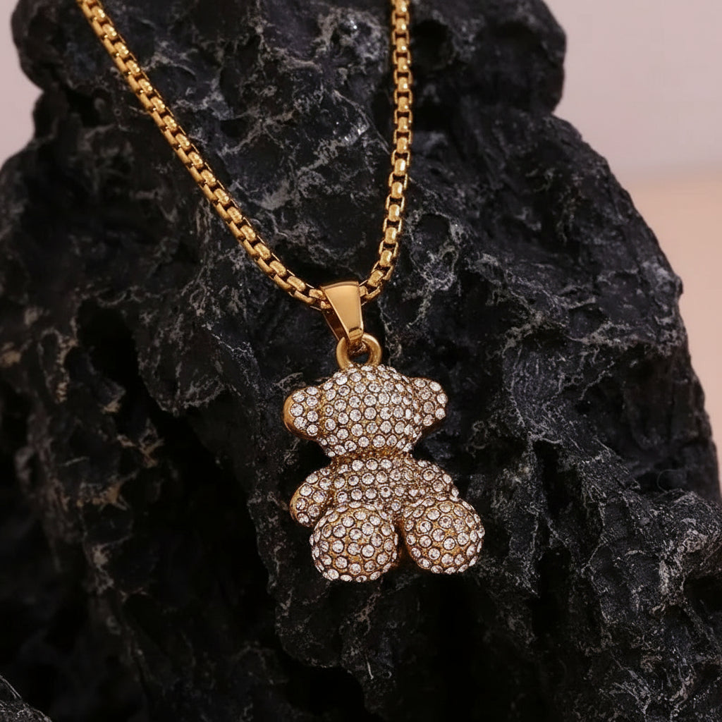 Gold sitting teddy bear with inlay stones pendant necklace on a textured black surface