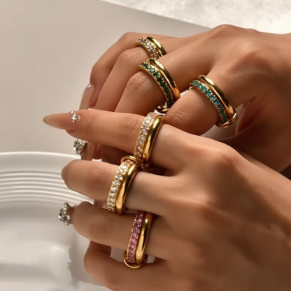 Close-up of hands wearing multiple rings with green and gold accents.