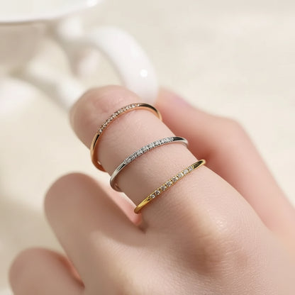 Close-up of a hand wearing a gold, silver and rose gold ring with stones on a light background