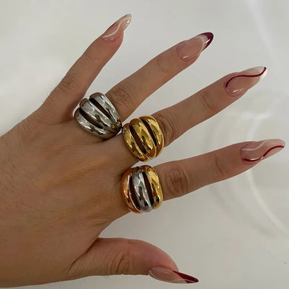 Hand wearing three gold and silver rings on a plain background