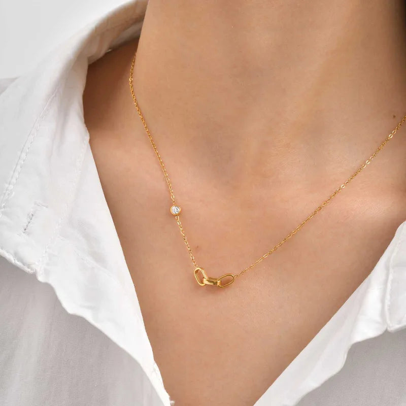 Gold necklace with a dainty 3 interlocked links pendant on a person wearing a white shirt.