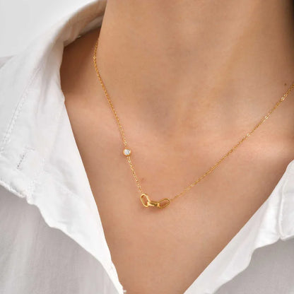 Gold necklace with a dainty 3 interlocked links pendant on a person wearing a white shirt.