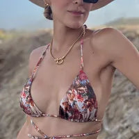 Gold necklace with horseshoe lock pendant on a woman in a colorful bikini and sun hat on a beach
