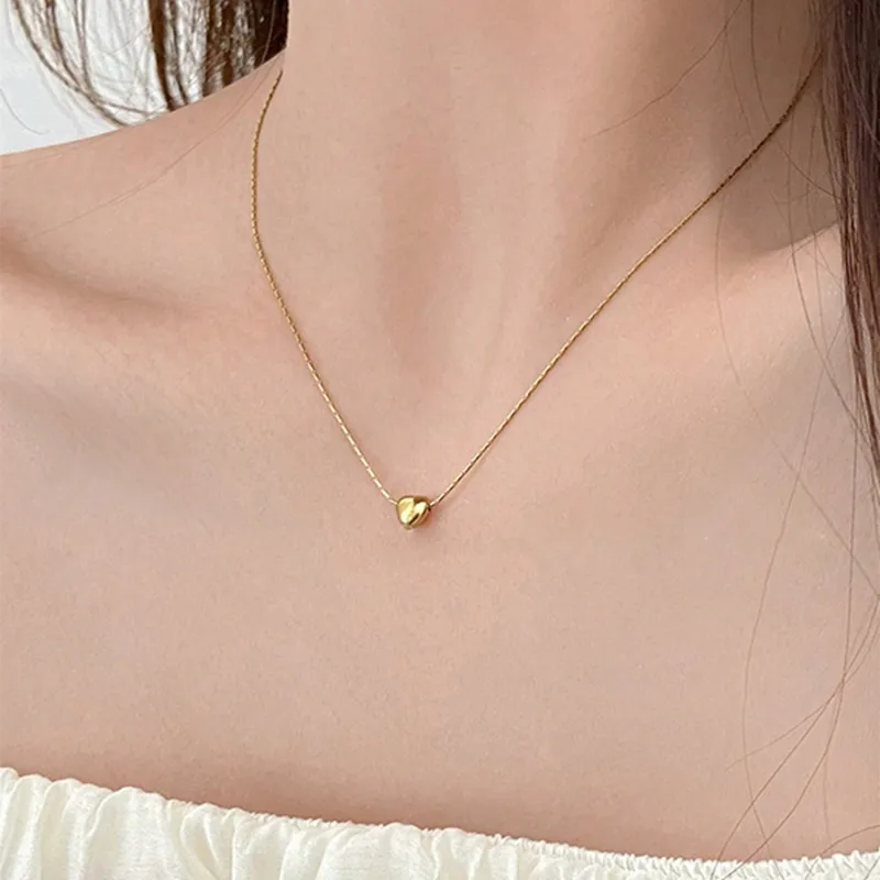 Gold heart-shaped necklace on a person wearing a white top
