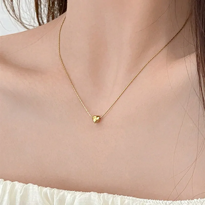 Gold heart-shaped necklace on a person wearing a white top