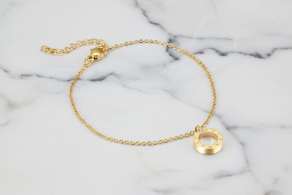 Gold bracelet with a circular pendant on a marble background
