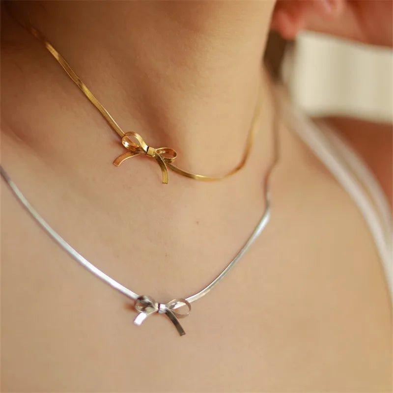 Gold necklace and silver necklace  both with bow pendants on a person's neck.