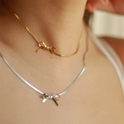 Gold necklace and silver necklace  both with bow pendants on a person's neck.