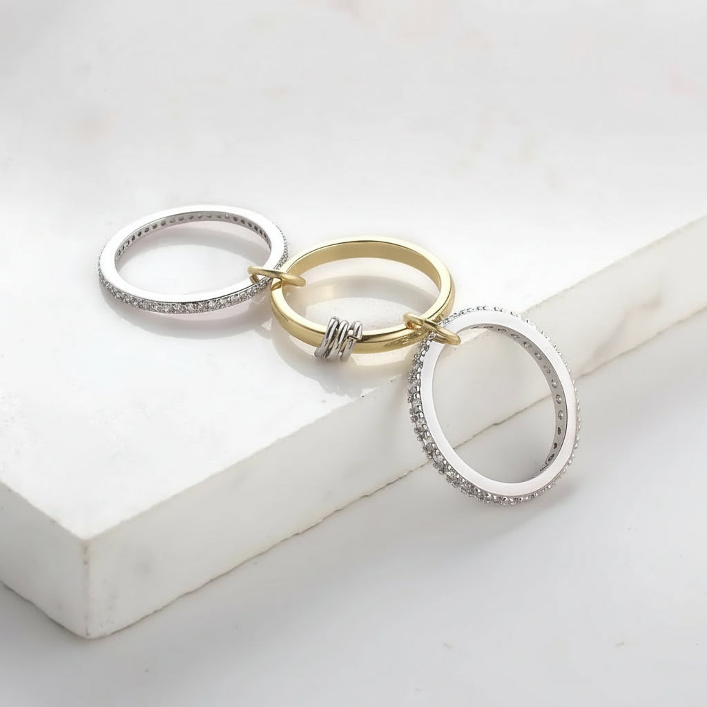 Three rings in gold and silver linked by 4 small silver and gold rings with CZ accents on a white surface