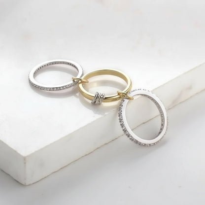 Three rings in gold and silver linked by 4 small silver and gold rings with CZ accents on a white surface