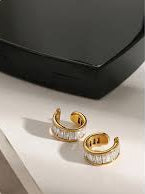 Gold ear cuffs on a reflective surface with a black box in the background