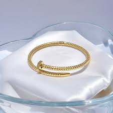 Gold nail bracelet on a white cloth with a clear glass container