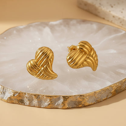 gold earrings shaped as elongated heart with lines on white quartz jewelry tray
