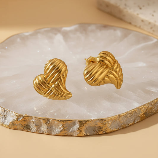 gold earrings shaped as elongated heart with lines on white quartz jewelry tray
