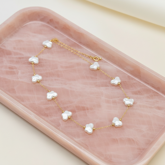 A gold chain necklace with nine white, flower-shaped freshwater pearls, displayed on a green marbled tray.