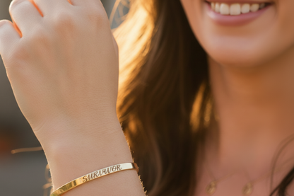 A close-up lifestyle shot of a woman's wrist wearing a gold band engraved  bracelet.