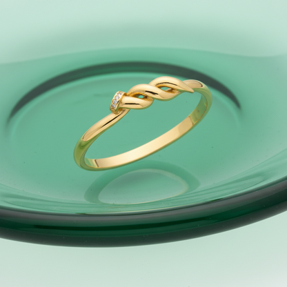 A polished yellow gold ring featuring a twisted knot design with a small inset diamond on the top, shown on a clean white background.