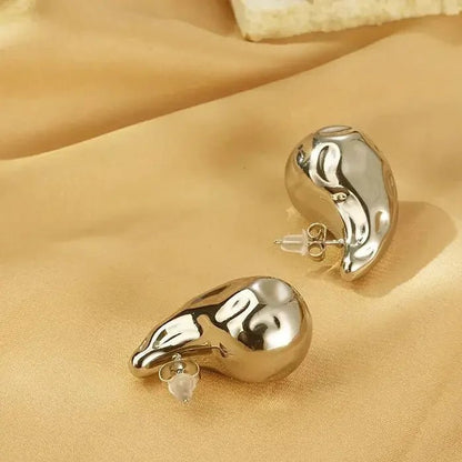 Metal Content 18K gold plated teardrop earrings with shiny curved design on beige fabric